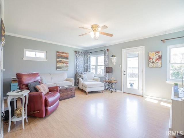 living area featuring light wood finished floors, a ceiling fan, crown molding, and baseboards