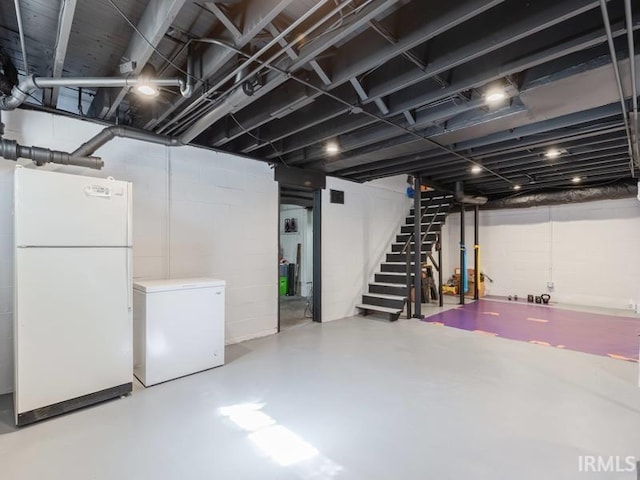 finished basement featuring stairs, freestanding refrigerator, and fridge