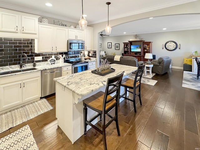 kitchen with a sink, tasteful backsplash, open floor plan, appliances with stainless steel finishes, and dark wood-style flooring