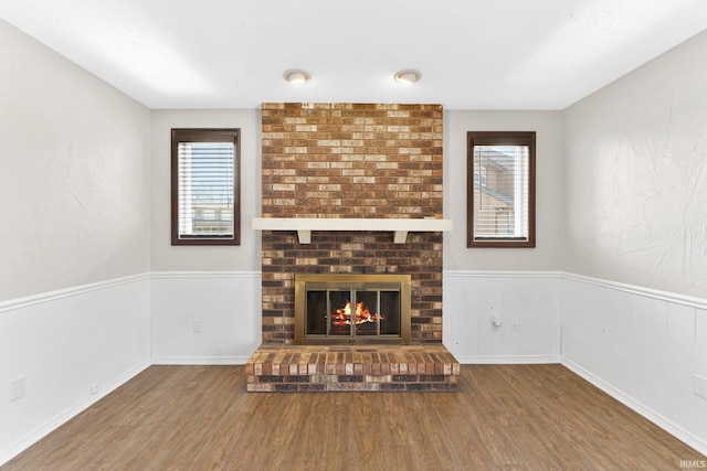 unfurnished living room featuring a wainscoted wall, a brick fireplace, and wood finished floors