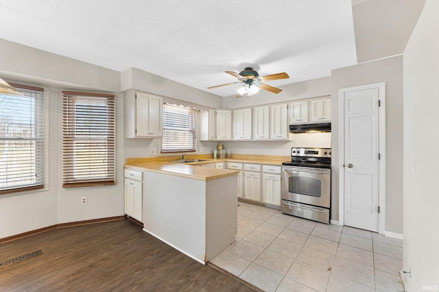 kitchen with under cabinet range hood, stainless steel electric range oven, light countertops, a peninsula, and a sink