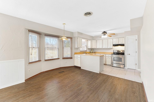 kitchen with visible vents, stainless steel electric range, light countertops, light wood-style floors, and under cabinet range hood