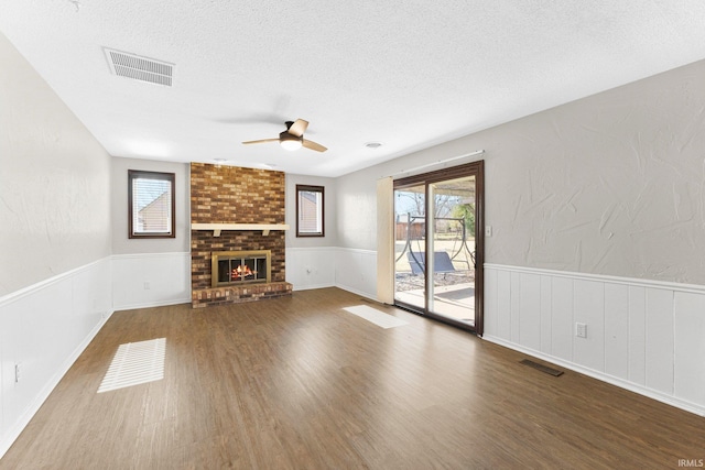 unfurnished living room featuring a brick fireplace, wood finished floors, visible vents, and a textured ceiling