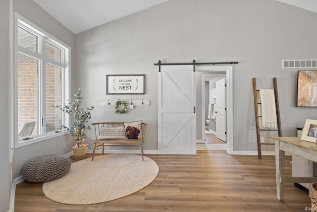 sitting room featuring a barn door, wood finished floors, visible vents, and baseboards