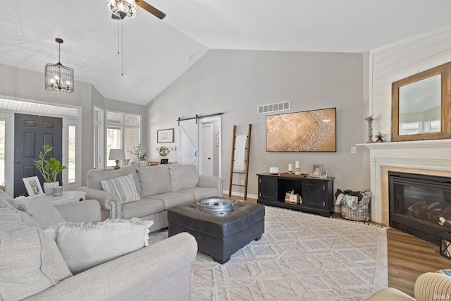 living area with wood finished floors, visible vents, high vaulted ceiling, ceiling fan, and a barn door