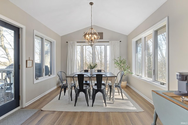 dining area with a notable chandelier, a healthy amount of sunlight, lofted ceiling, and wood finished floors