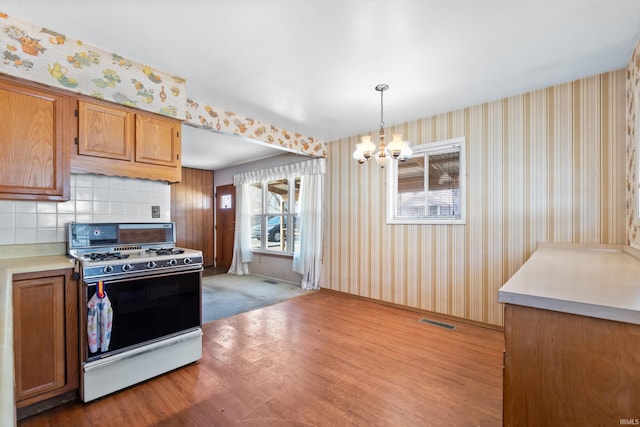 kitchen featuring wallpapered walls, wood finished floors, white gas range oven, and brown cabinets