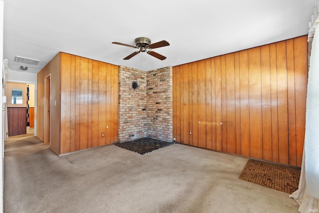 carpeted spare room with visible vents, wood walls, and ceiling fan