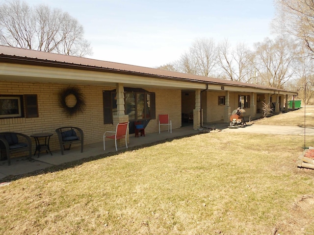 rear view of house featuring a patio area, a lawn, brick siding, and metal roof