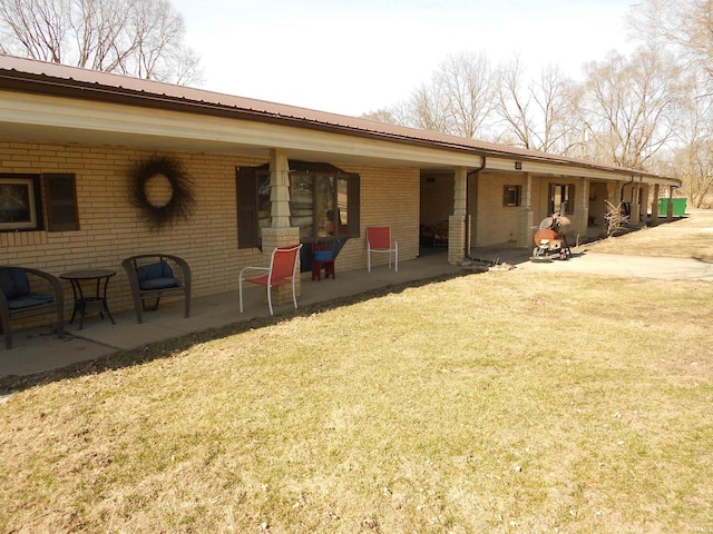 back of house with metal roof, brick siding, and a yard