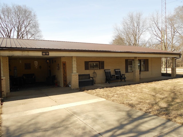 rear view of property featuring an attached carport, covered porch, concrete driveway, brick siding, and metal roof