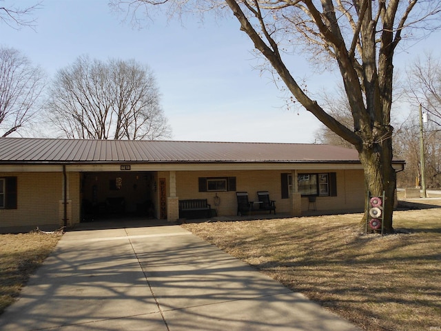 single story home with a porch, brick siding, driveway, and metal roof