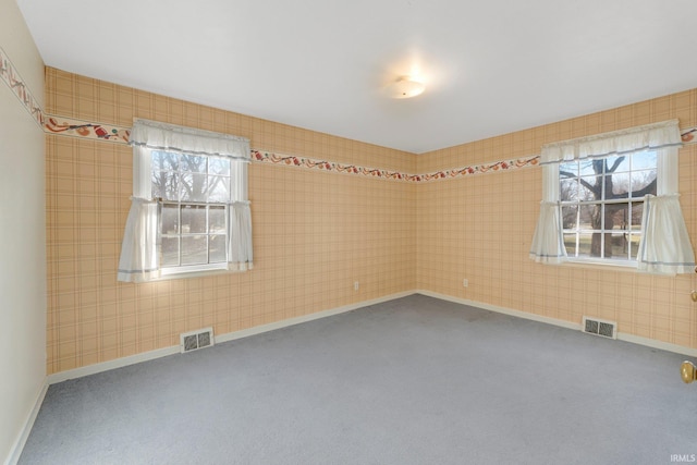 carpeted empty room featuring a healthy amount of sunlight, visible vents, and baseboards