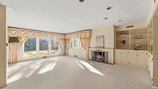 unfurnished living room featuring visible vents, light carpet, built in shelves, and a fireplace