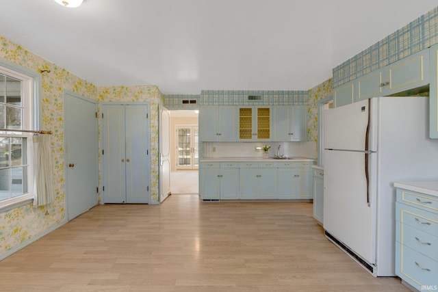 kitchen with a sink, wallpapered walls, freestanding refrigerator, light wood finished floors, and light countertops