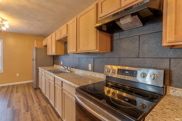 kitchen with baseboards, a sink, under cabinet range hood, appliances with stainless steel finishes, and backsplash