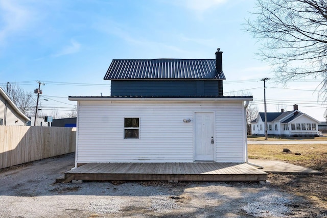 rear view of property featuring an outbuilding, fence, a chimney, and metal roof