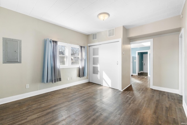 empty room featuring electric panel, visible vents, baseboards, and dark wood finished floors