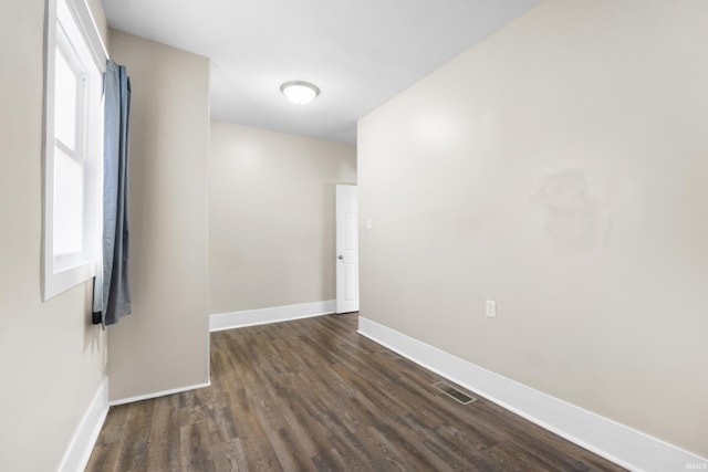 unfurnished room with a wealth of natural light, visible vents, dark wood-type flooring, and baseboards