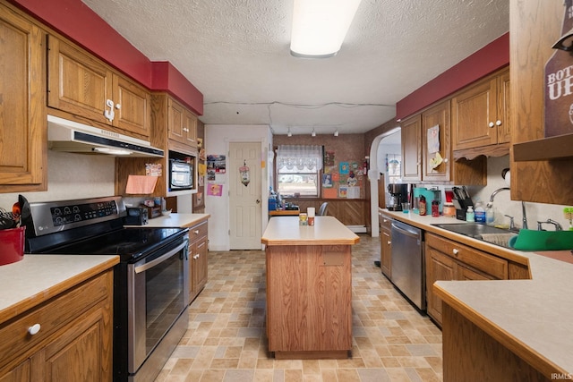 kitchen with arched walkways, a sink, stainless steel appliances, under cabinet range hood, and a center island