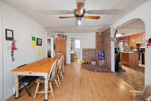 dining area with light wood-style flooring, a ceiling fan, arched walkways, and ornamental molding