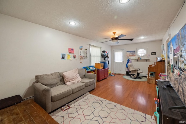 living area with ceiling fan, wood finished floors, a baseboard heating unit, and a textured ceiling