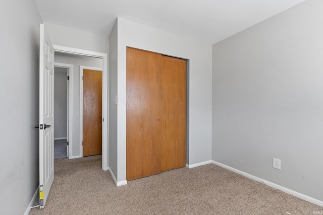 unfurnished bedroom featuring light carpet, baseboards, and a closet