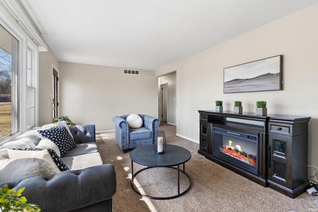 carpeted living area with a glass covered fireplace, baseboards, and visible vents