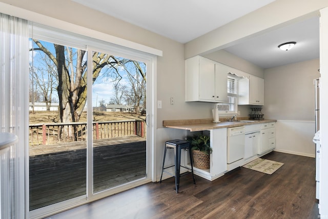 kitchen featuring white dishwasher, a sink, dark wood-type flooring, stove, and white cabinetry