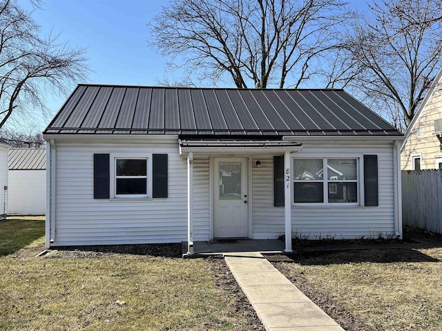 bungalow-style home with metal roof, fence, a front lawn, and a standing seam roof