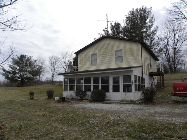 rear view of house with a chimney, a yard, and a sunroom