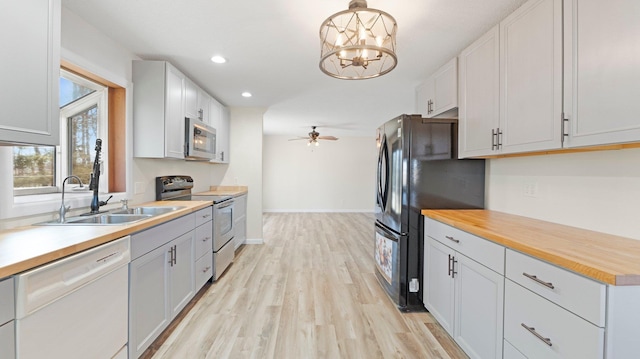 kitchen featuring light wood finished floors, wooden counters, recessed lighting, ceiling fan with notable chandelier, and appliances with stainless steel finishes