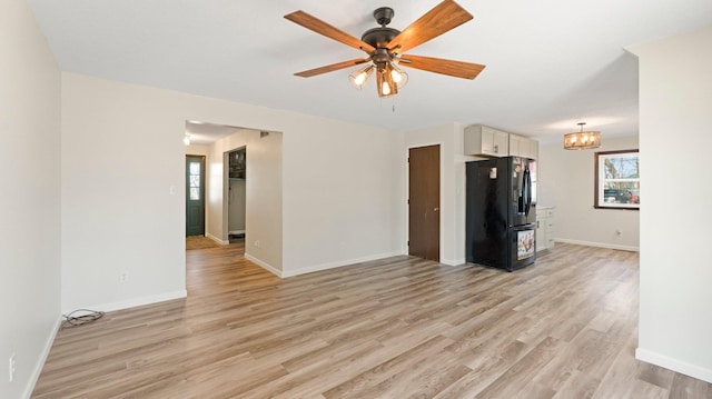 unfurnished living room featuring ceiling fan with notable chandelier, light wood-type flooring, and baseboards