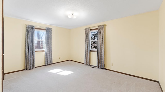 empty room featuring visible vents, a healthy amount of sunlight, carpet flooring, and baseboards