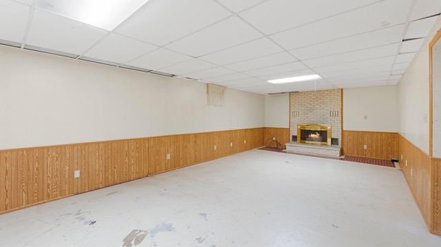 finished below grade area with a drop ceiling, wooden walls, a brick fireplace, and wainscoting