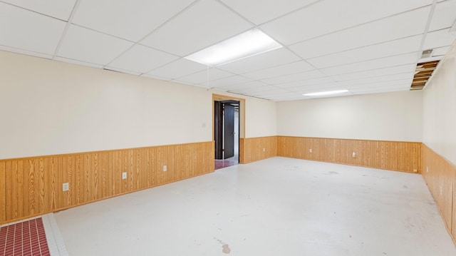 unfurnished room with a paneled ceiling, concrete floors, wood walls, and wainscoting