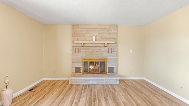 unfurnished living room featuring a stone fireplace, wood finished floors, and baseboards