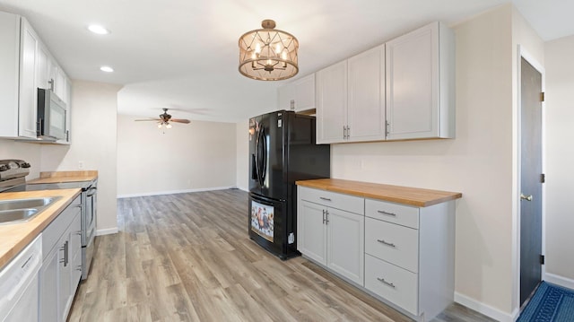 kitchen with baseboards, light wood finished floors, stainless steel appliances, wood counters, and ceiling fan with notable chandelier