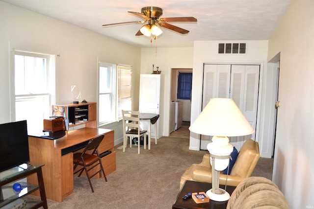 carpeted office space featuring visible vents, stacked washing maching and dryer, and a ceiling fan