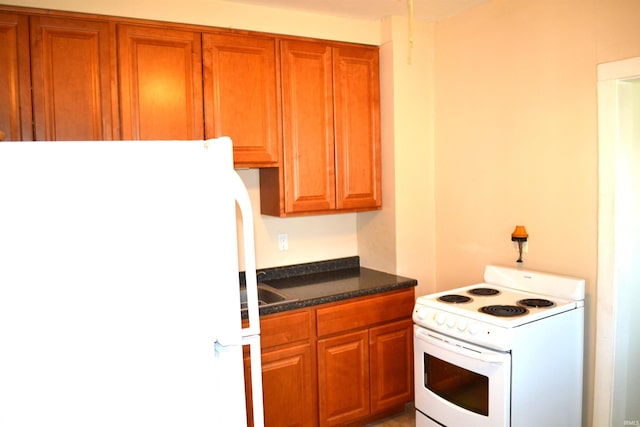 kitchen featuring dark stone counters, white appliances, and brown cabinets