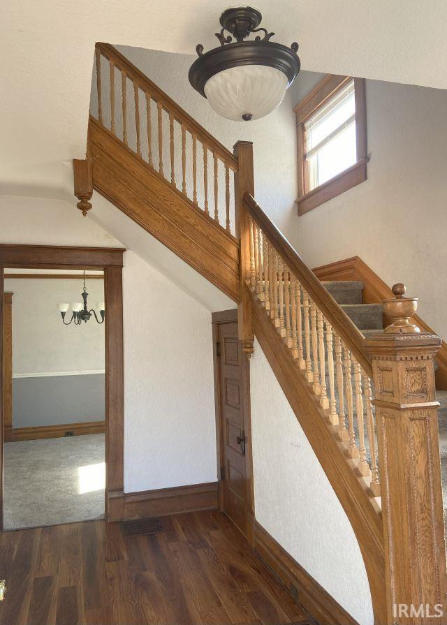 stairway with baseboards, an inviting chandelier, and wood finished floors