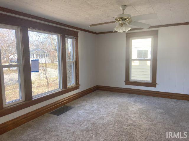 carpeted spare room featuring a ceiling fan, crown molding, baseboards, and visible vents