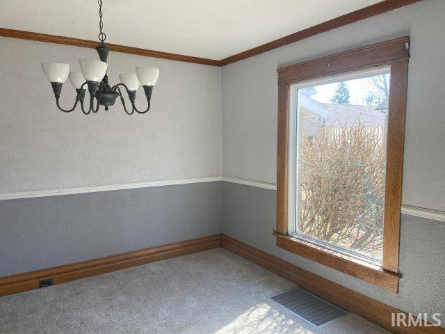 unfurnished dining area featuring baseboards, visible vents, ornamental molding, carpet flooring, and a notable chandelier