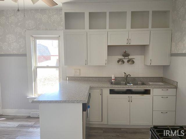 kitchen with a wainscoted wall, a peninsula, white cabinets, and wallpapered walls