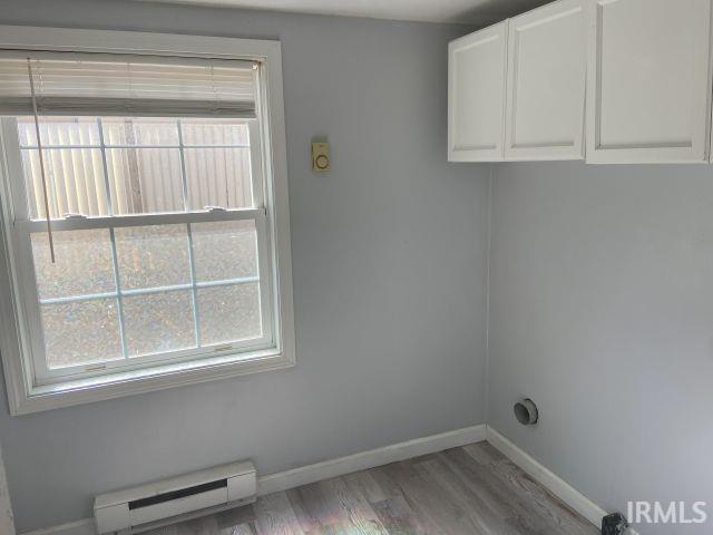 laundry room featuring wood finished floors, cabinet space, baseboards, and a baseboard radiator