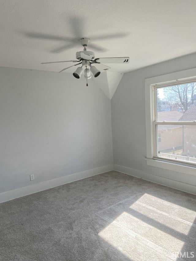 carpeted spare room featuring a textured ceiling, a ceiling fan, baseboards, and vaulted ceiling