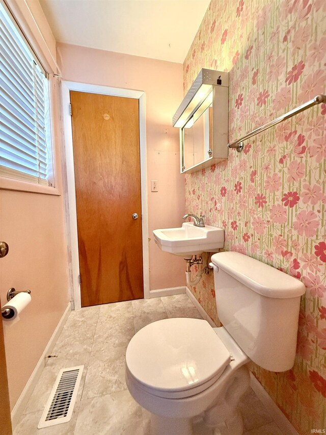 half bath featuring visible vents, wallpapered walls, baseboards, toilet, and a sink