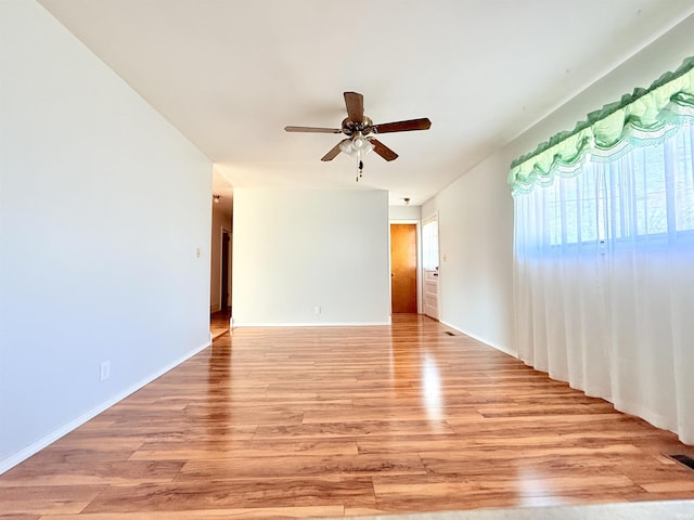 spare room with baseboards, light wood finished floors, and ceiling fan