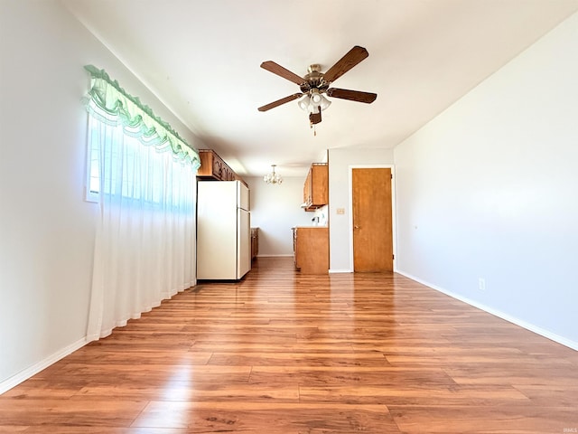 unfurnished living room featuring light wood-style flooring, ceiling fan with notable chandelier, and baseboards