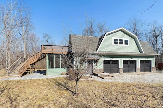 view of front facade featuring a gambrel roof, driveway, stone siding, stairway, and a sunroom